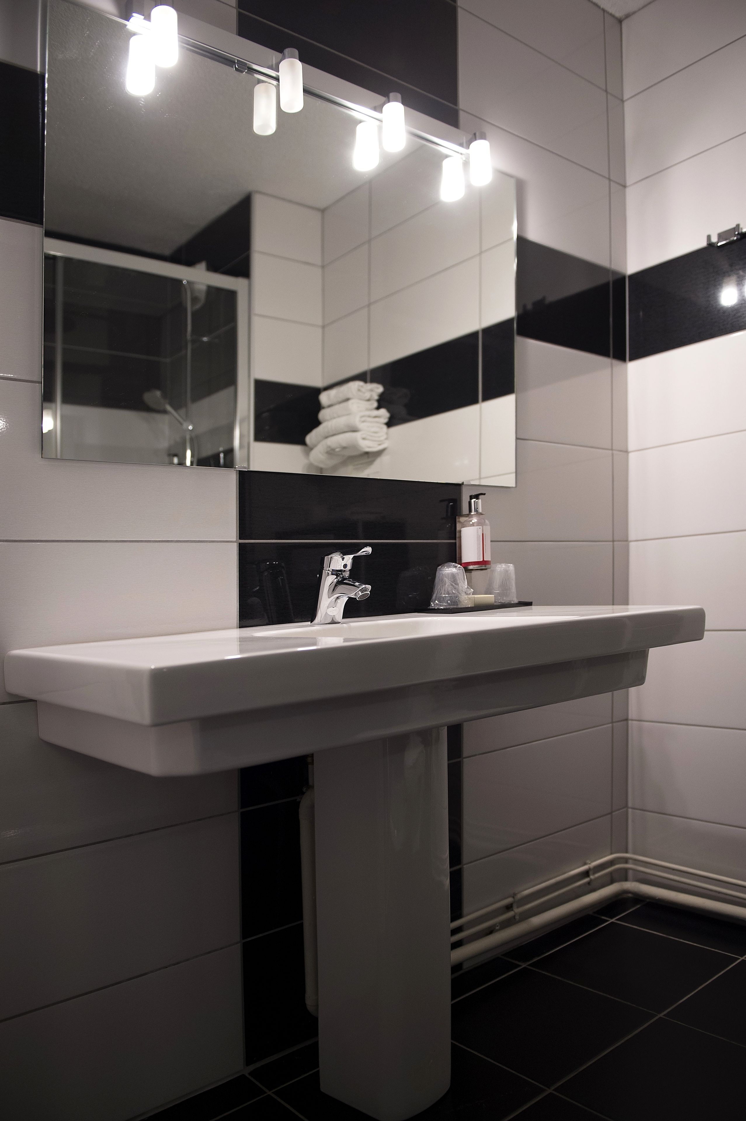Ein modernes Badezimmer mit einem weißen Waschbecken, einem beleuchteten Spiegel und schwarz-weißen Fliesen.