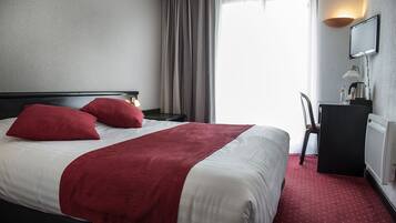 Une chambre d’hôtel équipée d’un lit, d’un bureau, d’une chaise, d’une lampe et d’un téléviseur.