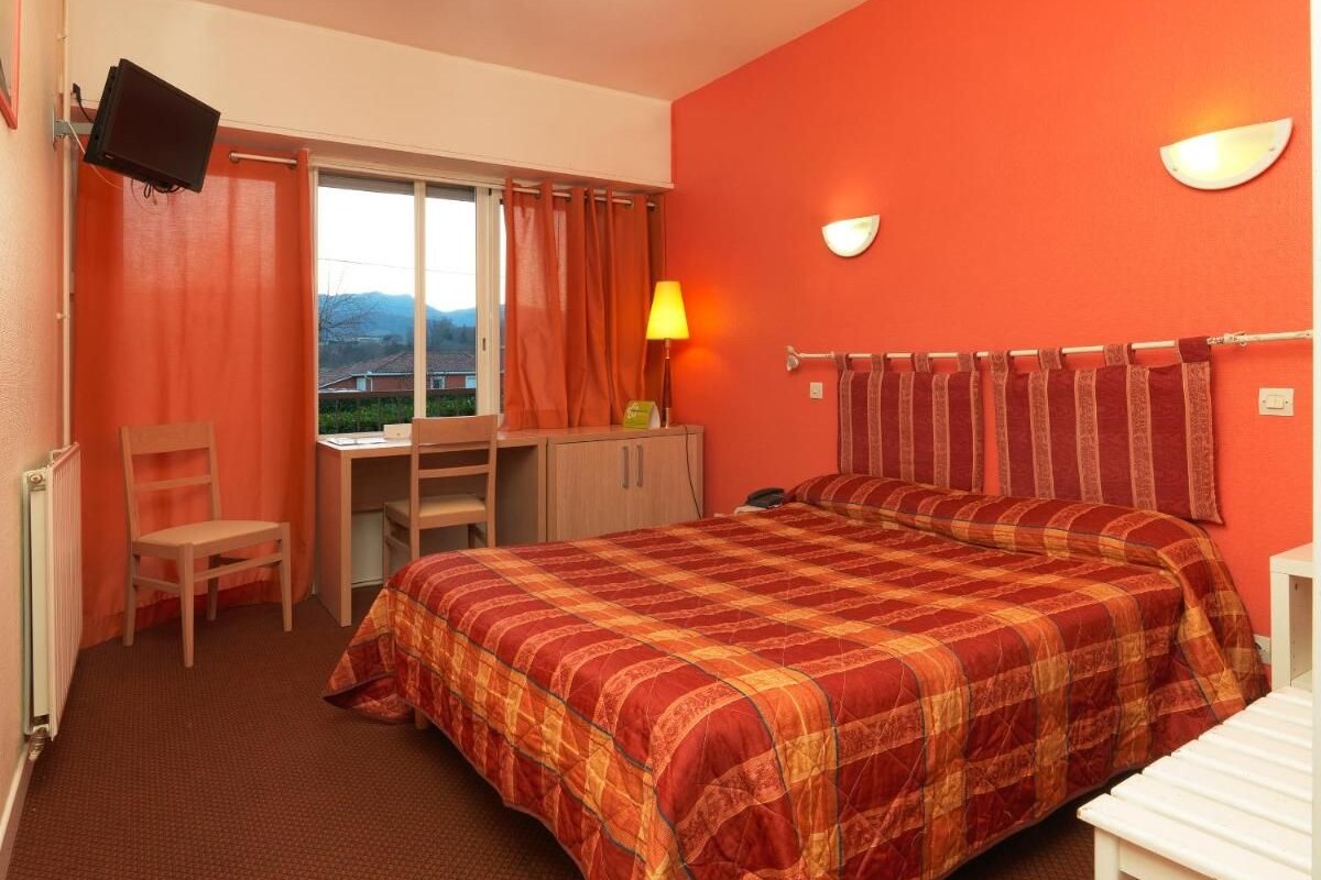 A hotel room with a bed, a desk, a chair, a TV, and a window with curtains.