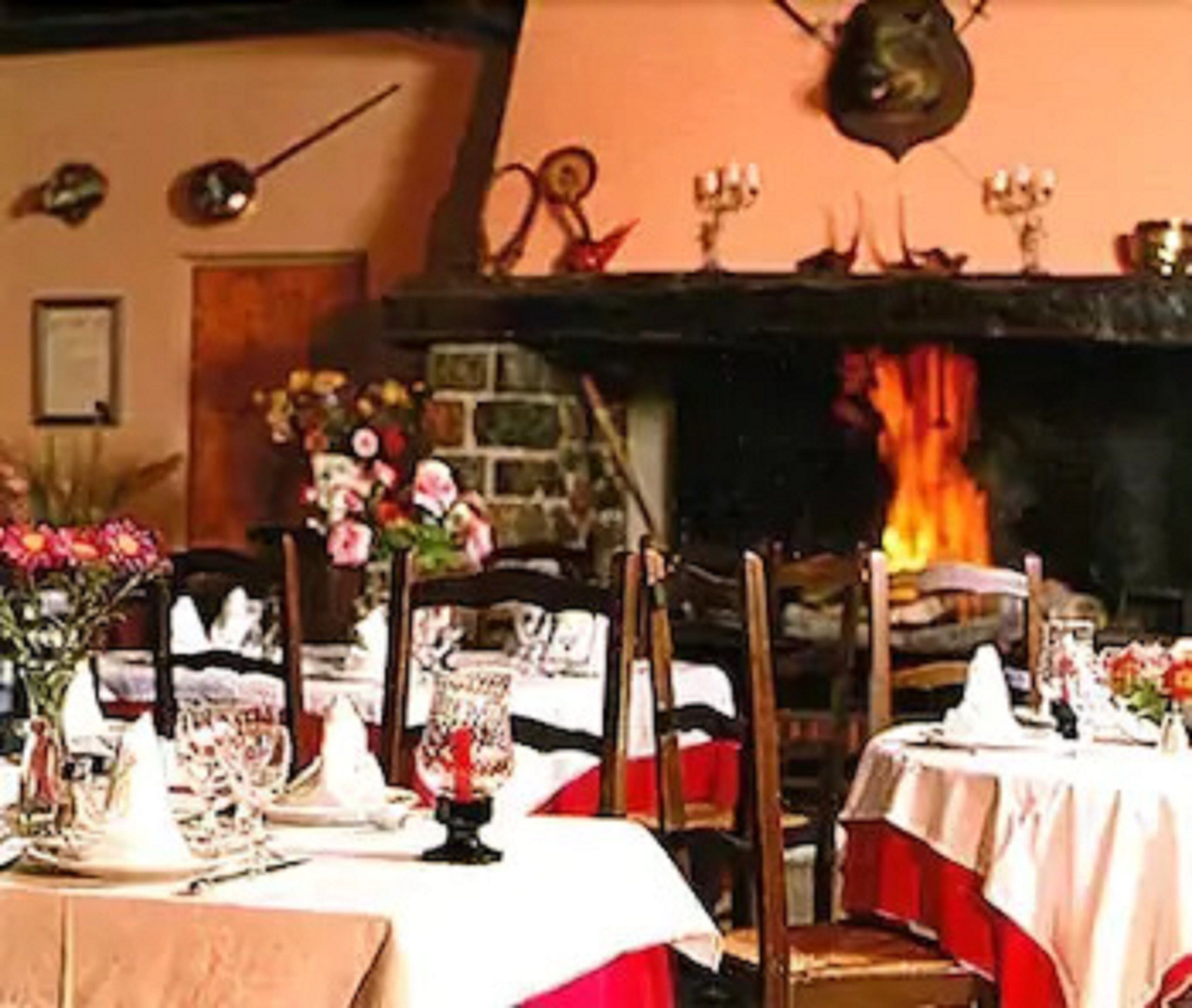 Un comedor con mesas dispuestas para una comida, una chimenea al fondo y un reloj montado en la pared.