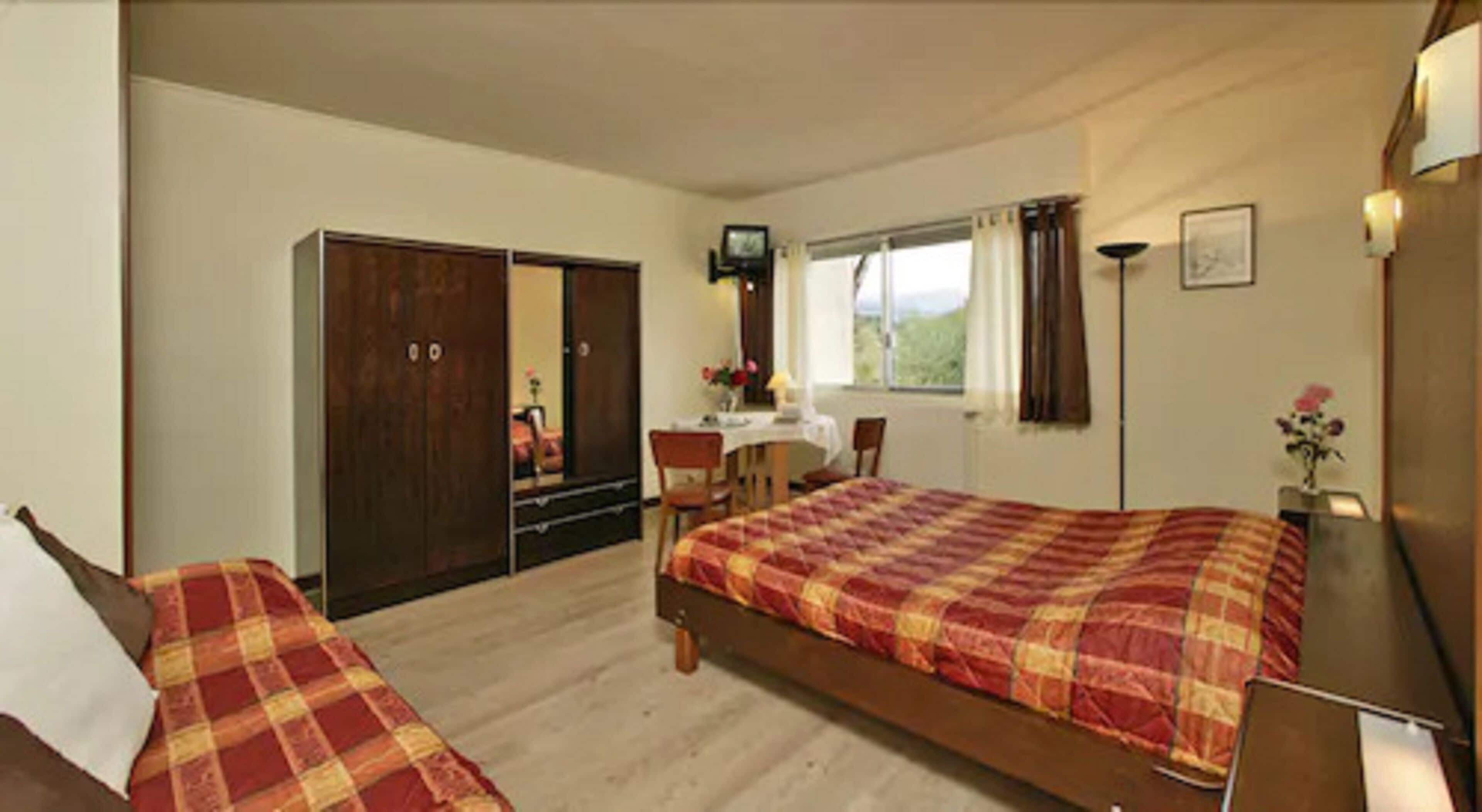 Une chambre avec deux lits, un bureau, une chaise, une armoire et un téléviseur.