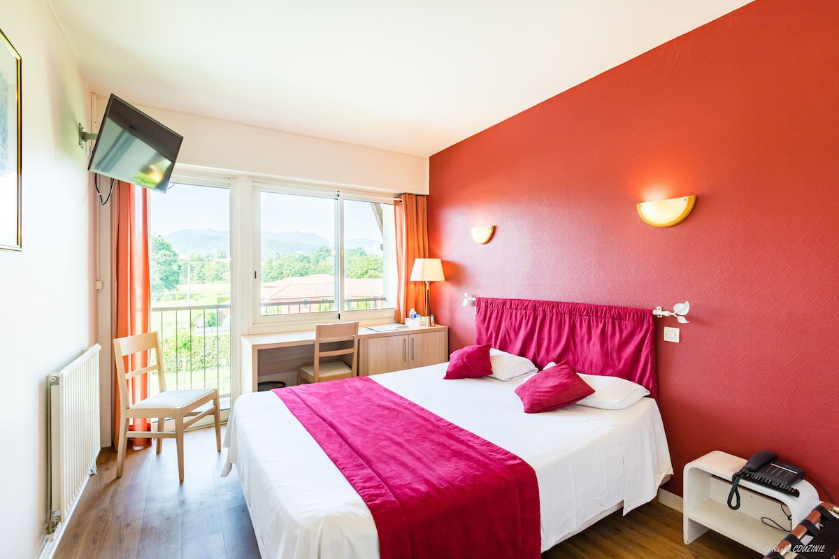 A hotel room with a bed, a desk, a chair, a TV, and a phone.