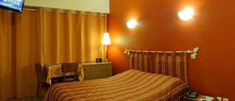 A hotel room with a bed, a desk, a chair, a television, and a lamp.