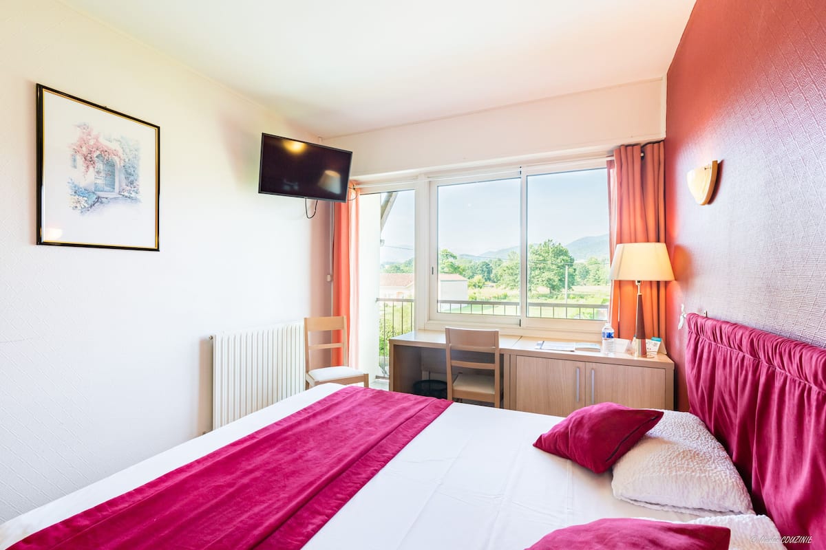 A hotel room with a bed, a desk, a chair, a TV, and a window with curtains.