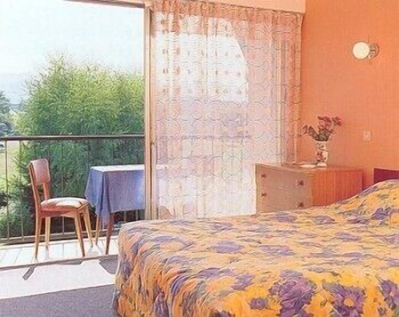 Um quarto com cama, uma cadeira, uma mesa e varanda.
