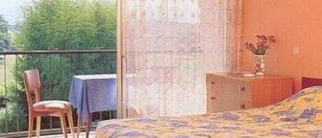 A bedroom with a bed, a chair, a table, and a balcony.