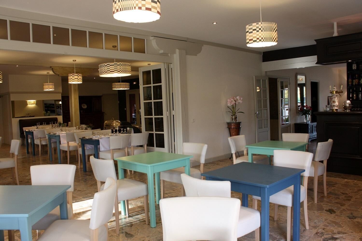Un comedor con mesas y sillas, una zona de cocina con barra, y un ventanal grande.