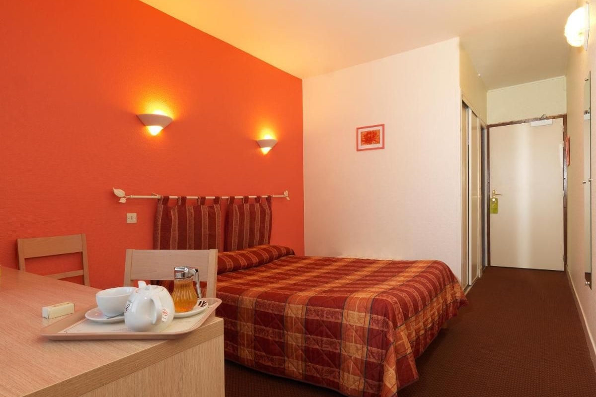 A hotel room with a bed, a desk with a tray of breakfast items, and two wall-mounted lights.