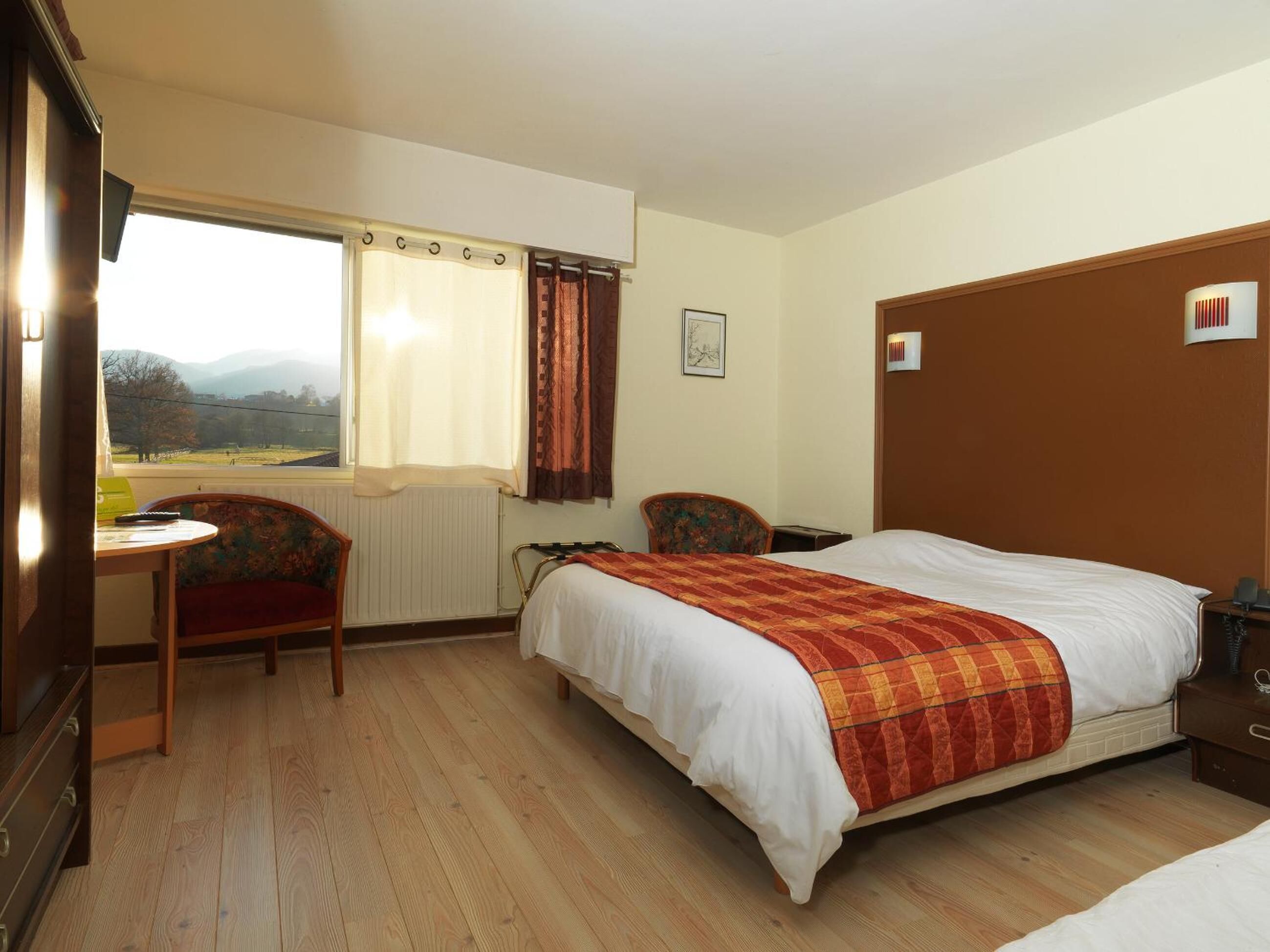 Una habitación de hotel con cama, escritorio, silla y ventana con cortinas.