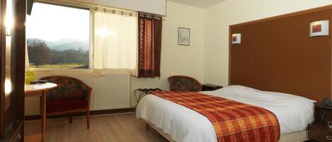 A hotel room with a bed, a desk, a chair, and a window with curtains.