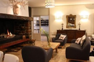 Una sala de estar acogedora con chimenea, dos sillones, una mesa de centro y una estantería al fondo.
