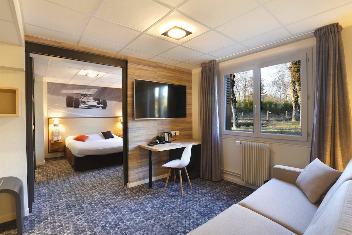 A hotel room with a bed, desk, chair, TV, and a window with curtains.