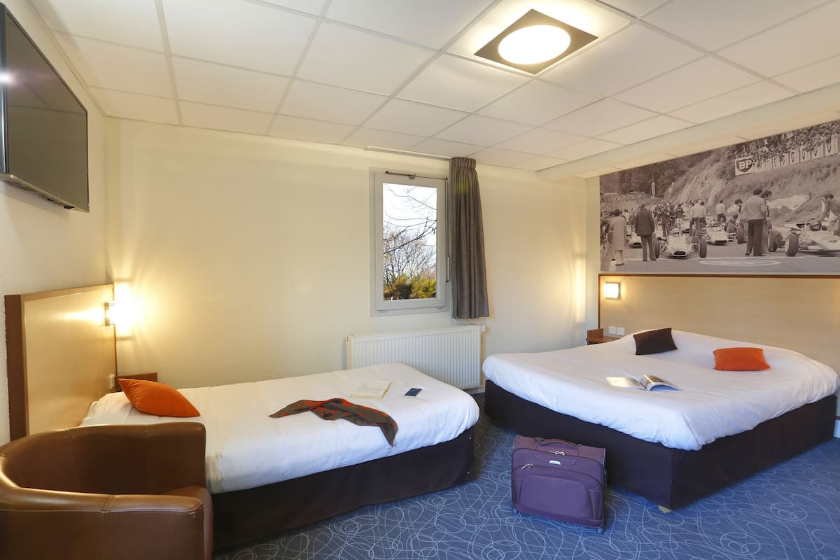 A hotel room with two beds, a flat-screen TV, a window with curtains, and a wall-mounted picture.