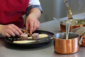 A person preparing food on a black plate with a copper pot nearby. - Le Relais des Puys (Orcines)