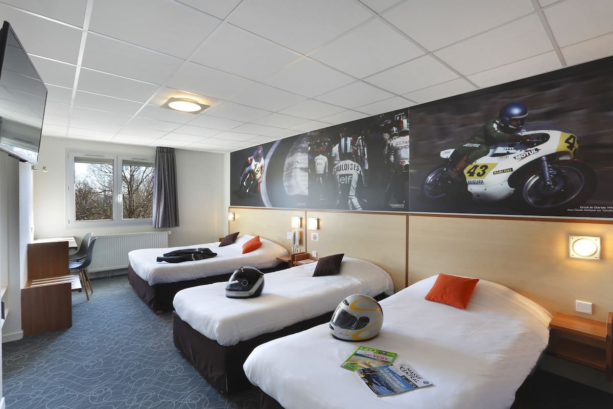 A hotel room with two beds, a desk, and a large motorcycle racing poster on the wall.
