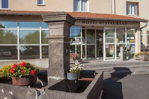 A hotel entrance with a sign reading "HOTEL RESTAURANT," a glass door, and a small planter with flowers. - Le Relais des Puys (Orcines)