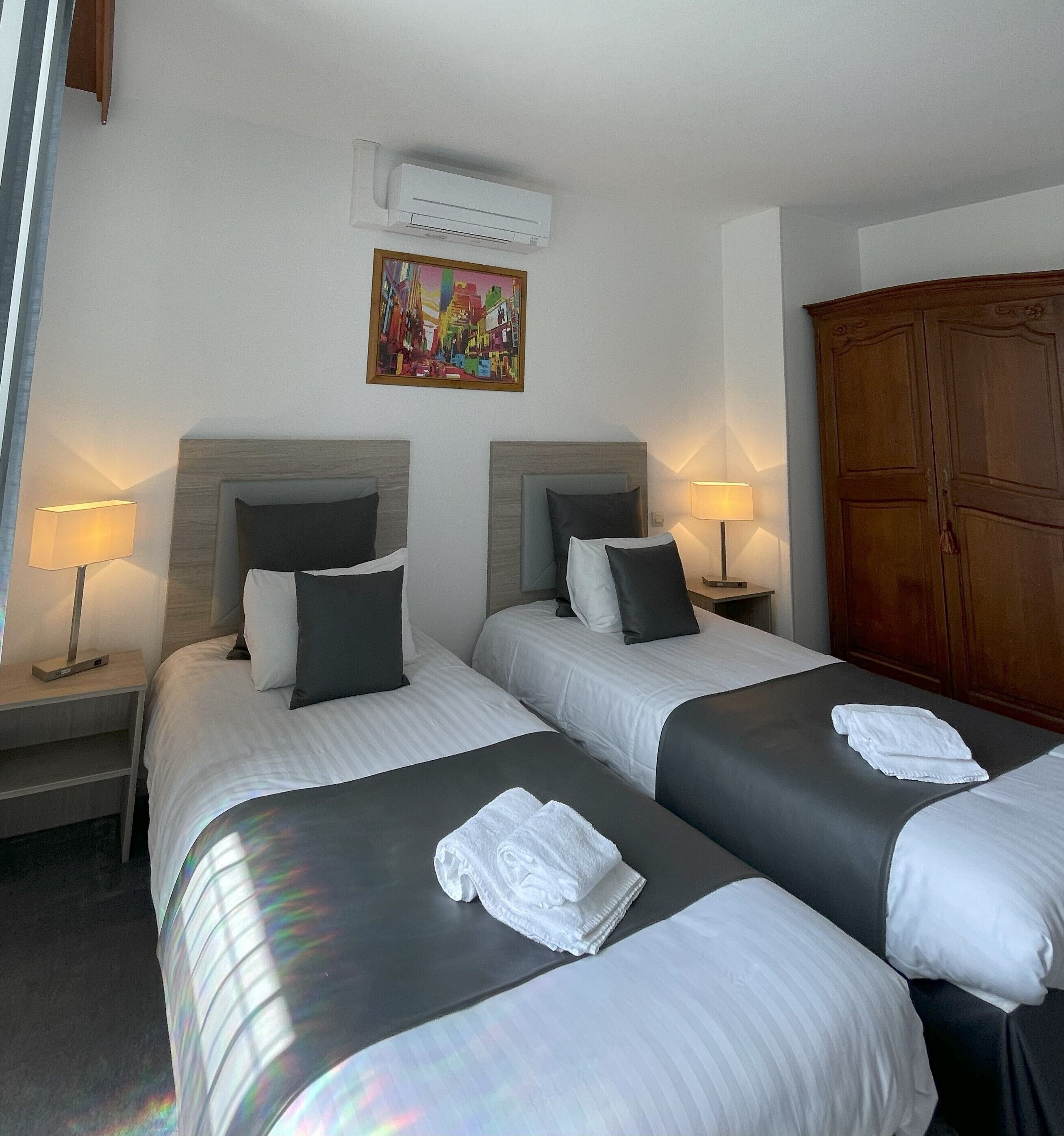 Une chambre d’hôtel avec deux lits, un tableau au mur, un climatiseur et une armoire.