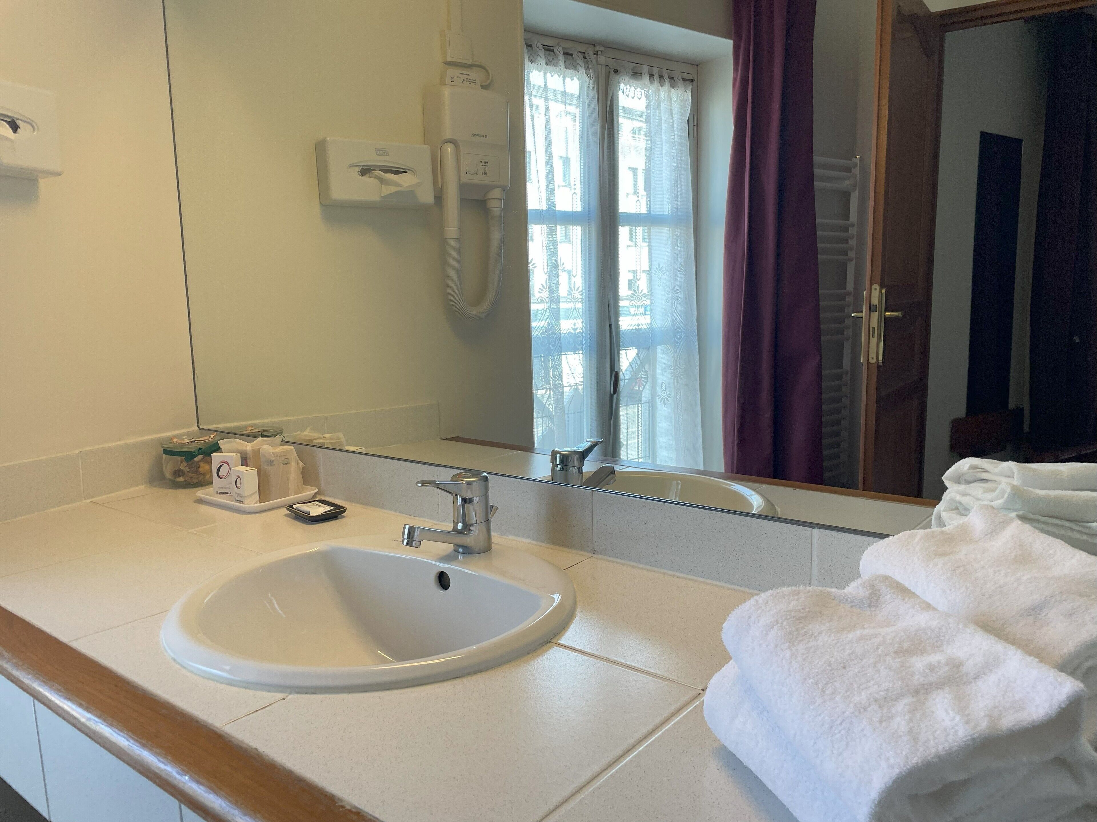 A bathroom with a sink, mirror, towel rack, and a window with curtains.