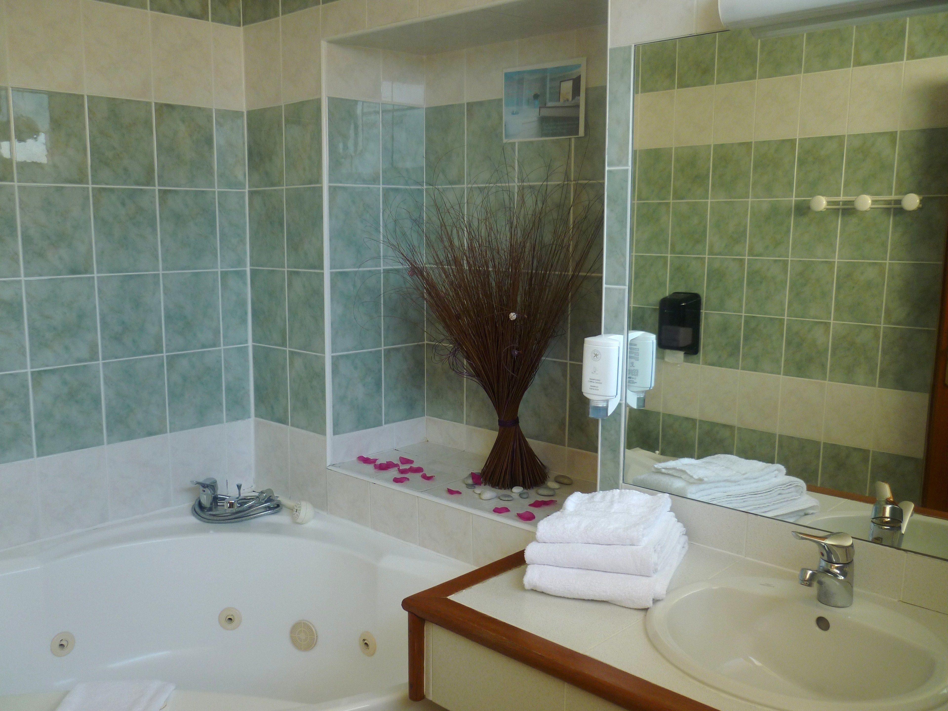A bathroom with a bathtub, a sink, a mirror, and a wall-mounted soap dispenser.