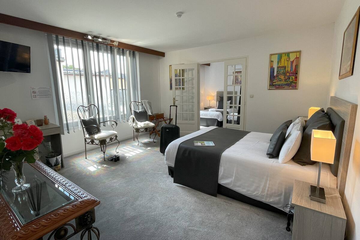 Una habitación de hotel con cama, escritorio, silla, televisión y ventana con cortinas.