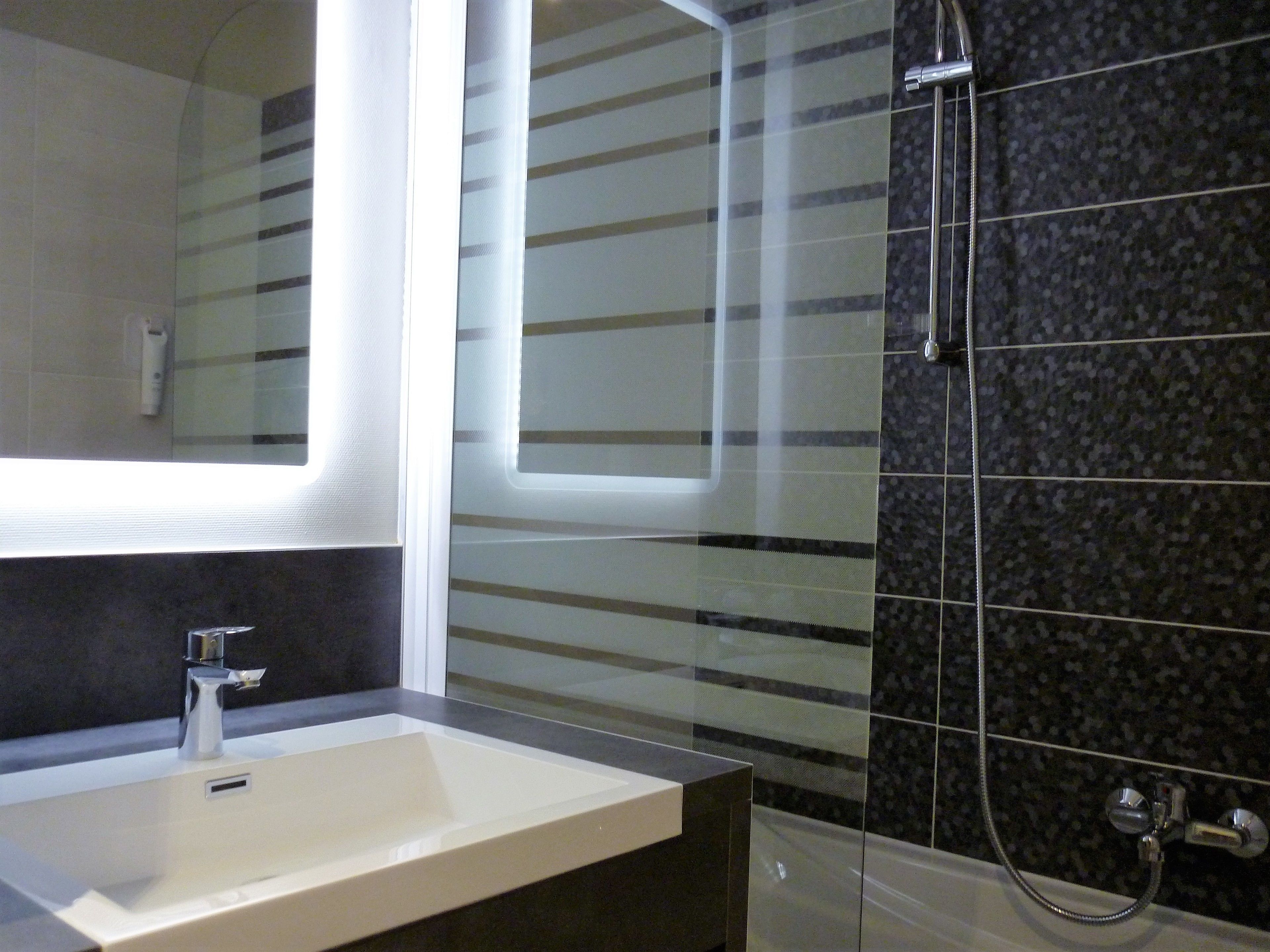 A modern bathroom with a white sink, a mirror, and a shower with a dark tiled wall.