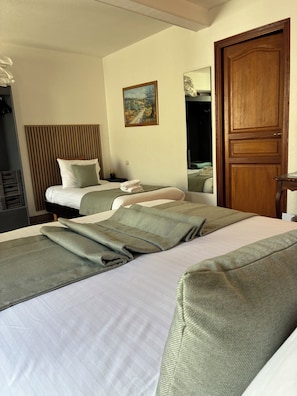 Una habitación de hotel con dos camas, una puerta de madera, un cuadro en la pared y un espejo.