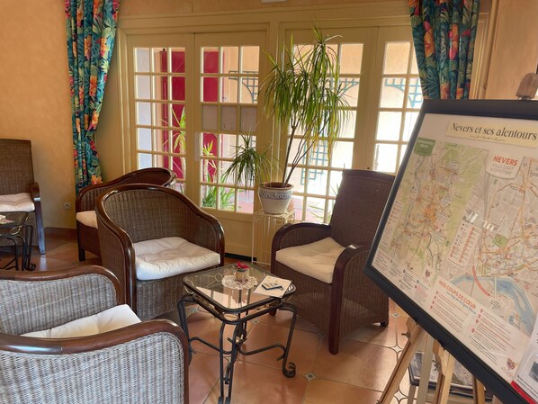 A cozy room with wicker furniture, a glass table, and a map on the wall. - The Originals Boutique, Hôtel Clos St Marie (Nevers)