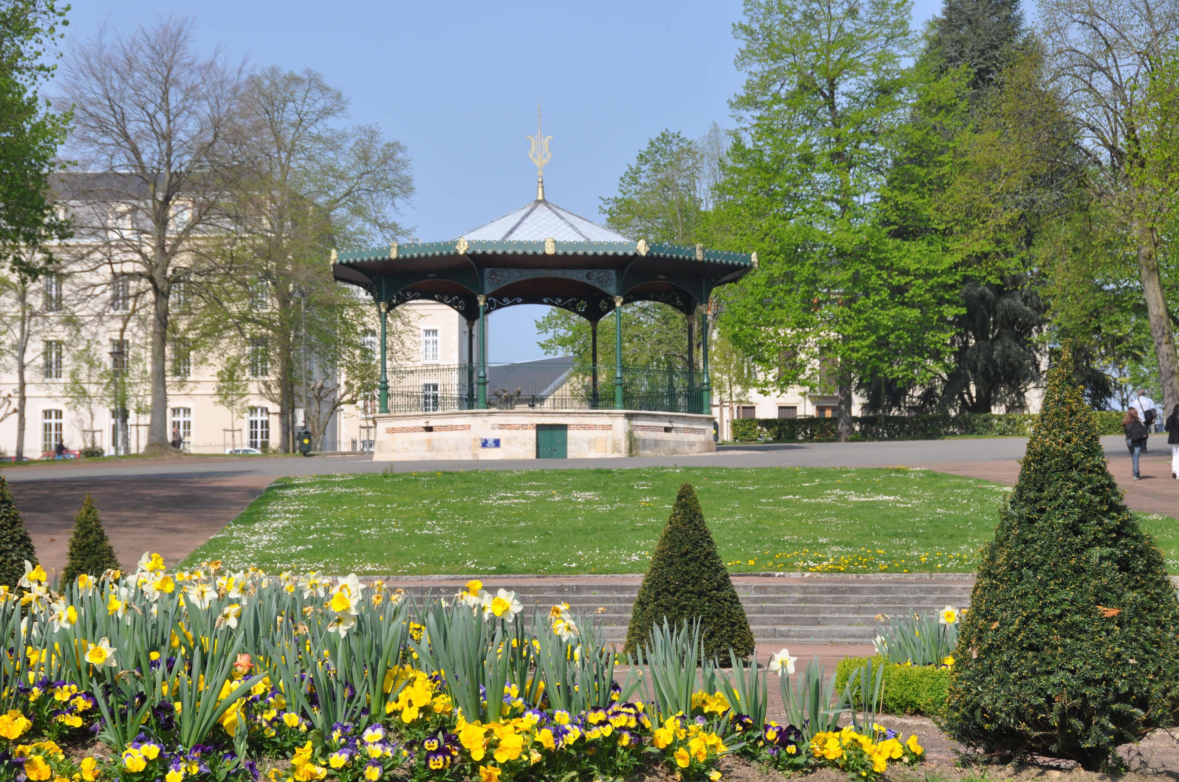 A gazebo in a park with a lawn and flowers.