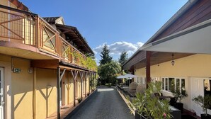 A courtyard with a gravel path, yellow buildings, and potted plants. - The Originals Boutique, Hôtel Clos St Marie (Nevers)