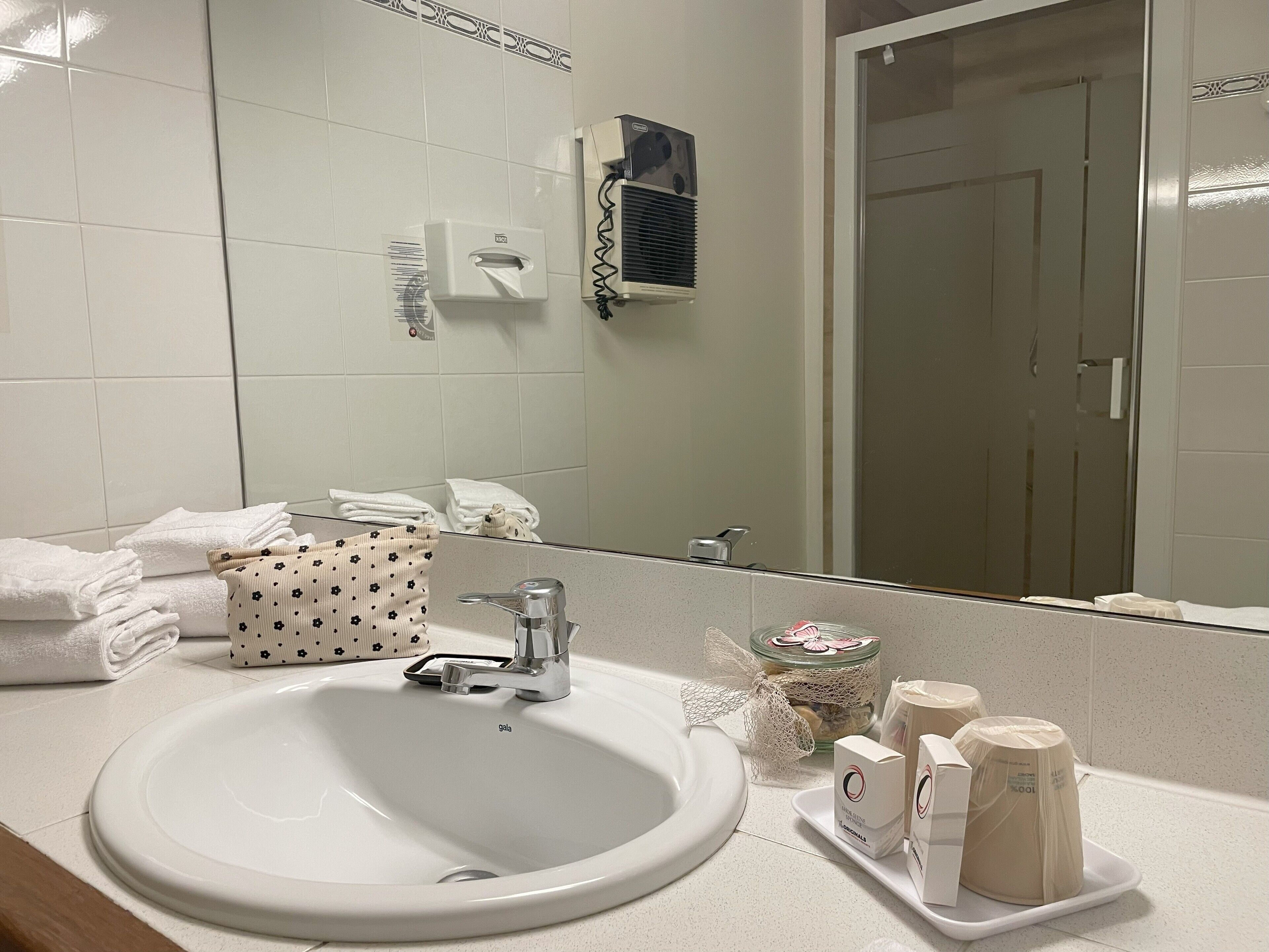 A bathroom with a white sink, a mirror, a towel rack, and a glass jar with a net.