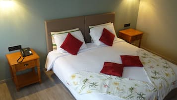 Una cama bien hecha con ropa de cama blanca y almohadas rojas, un teléfono en la mesita de noche y dos mesitas de noche con lámparas.