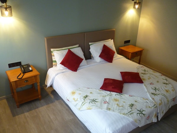 A neatly made bed with white bedding and red pillows, a bedside telephone, and two nightstands with lamps.