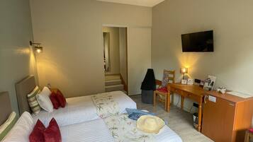 A hotel room with two beds, a desk, a chair, a television, and a staircase leading to another room.