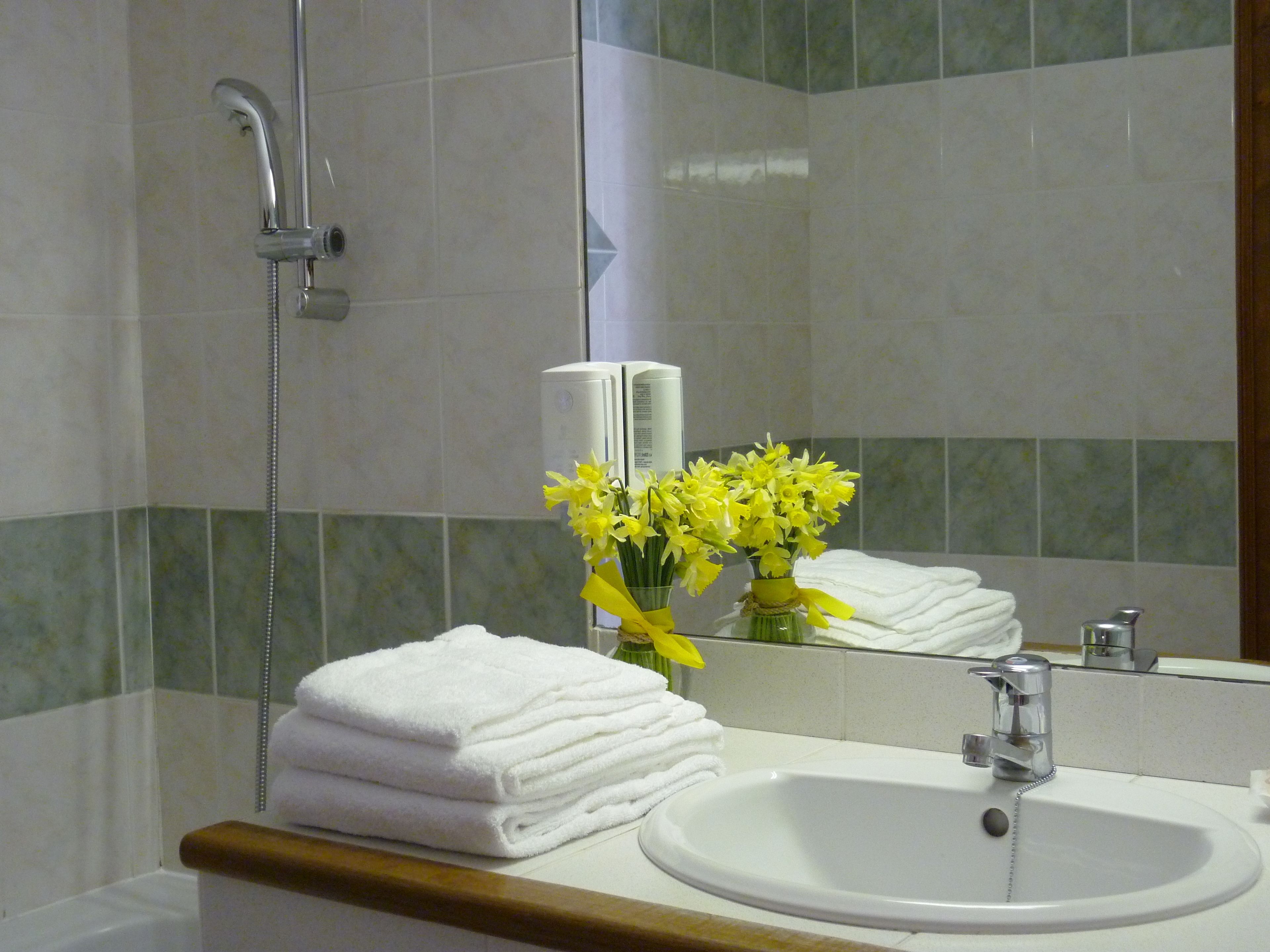 Un baño con lavamanos, espejo y una pila de toallas blancas.