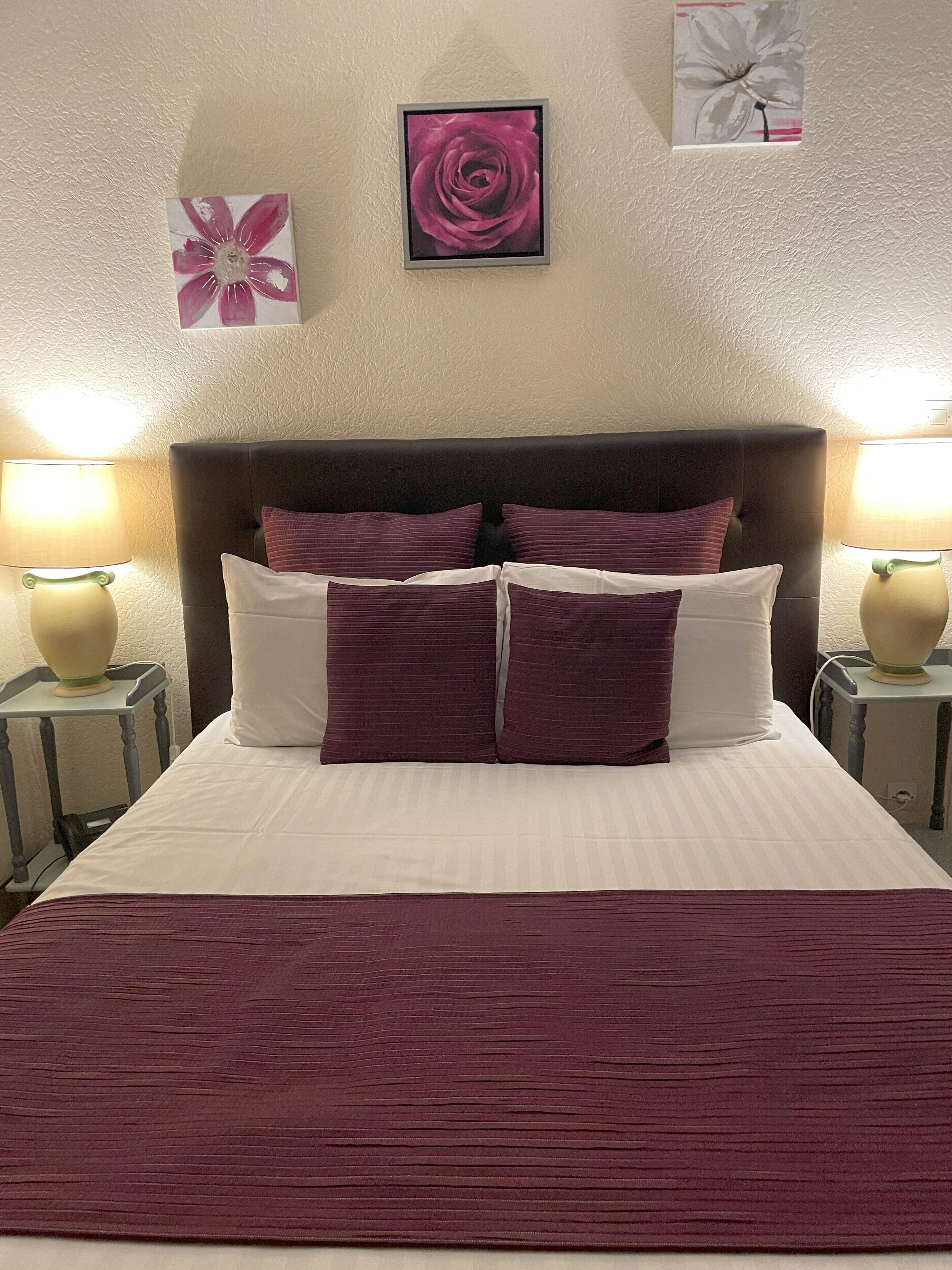 A neatly made bed with a dark headboard, two bedside lamps, and three pillows.
