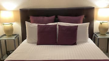 A neatly made bed with a dark headboard, two bedside lamps, and three pillows.