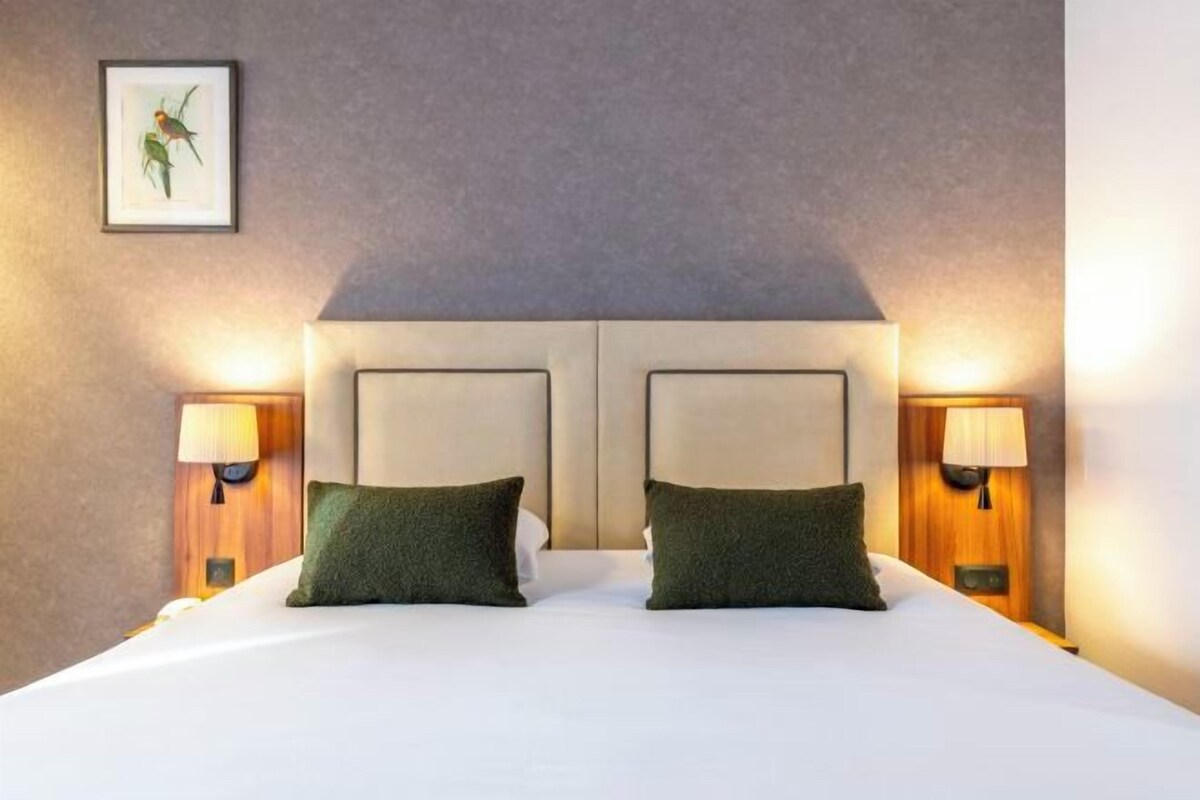 Une chambre d’hôtel avec un grand lit, deux lampes de chevet et un tableau encadré au mur.
