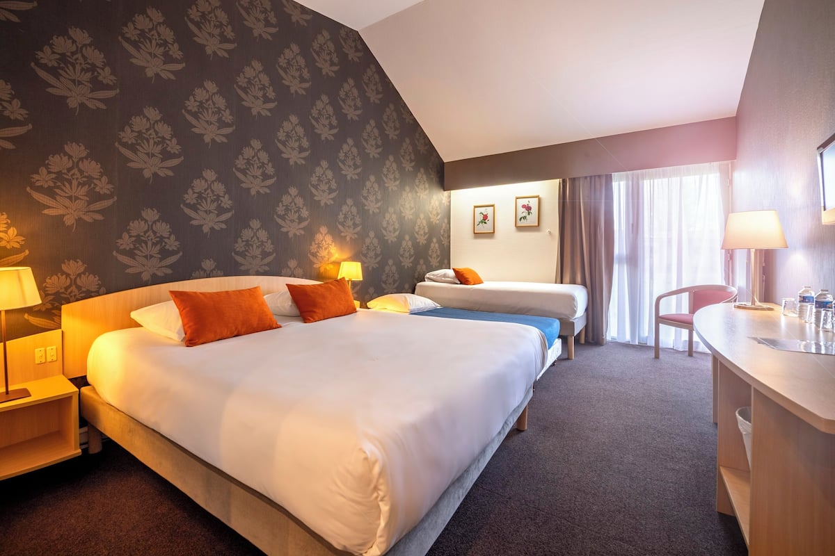 Une chambre d’hôtel avec deux lits, un bureau, une chaise, une lampe et une fenêtre avec des rideaux.