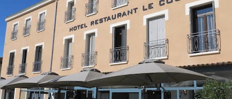A hotel with the sign "HOTEL RESTAURANT LE COURS" and outdoor seating with umbrellas.