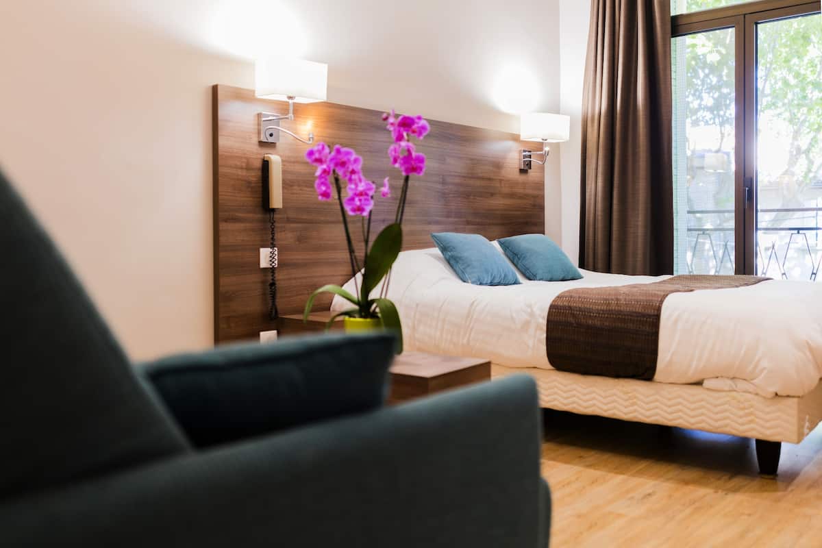 A hotel room with a bed, two pillows, a bedside table, a lamp, and a window with curtains.