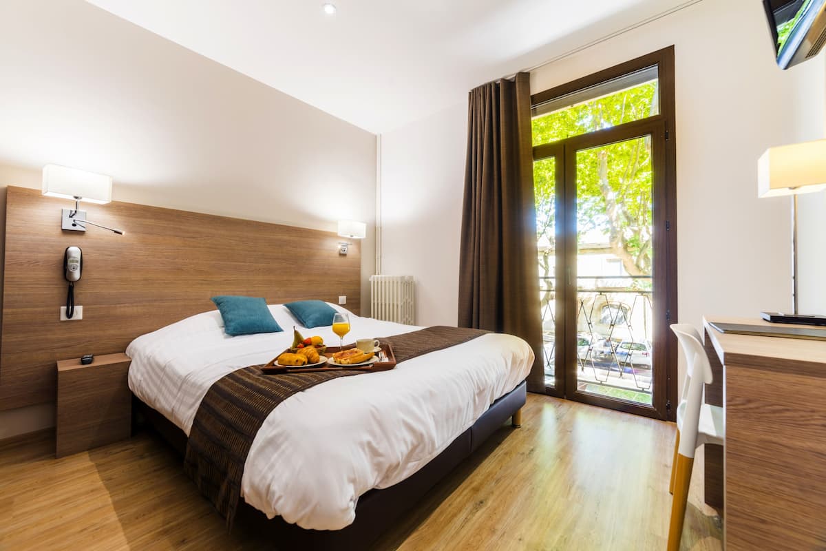 A hotel room with a bed, bedside table, lamp, and a desk with a chair.