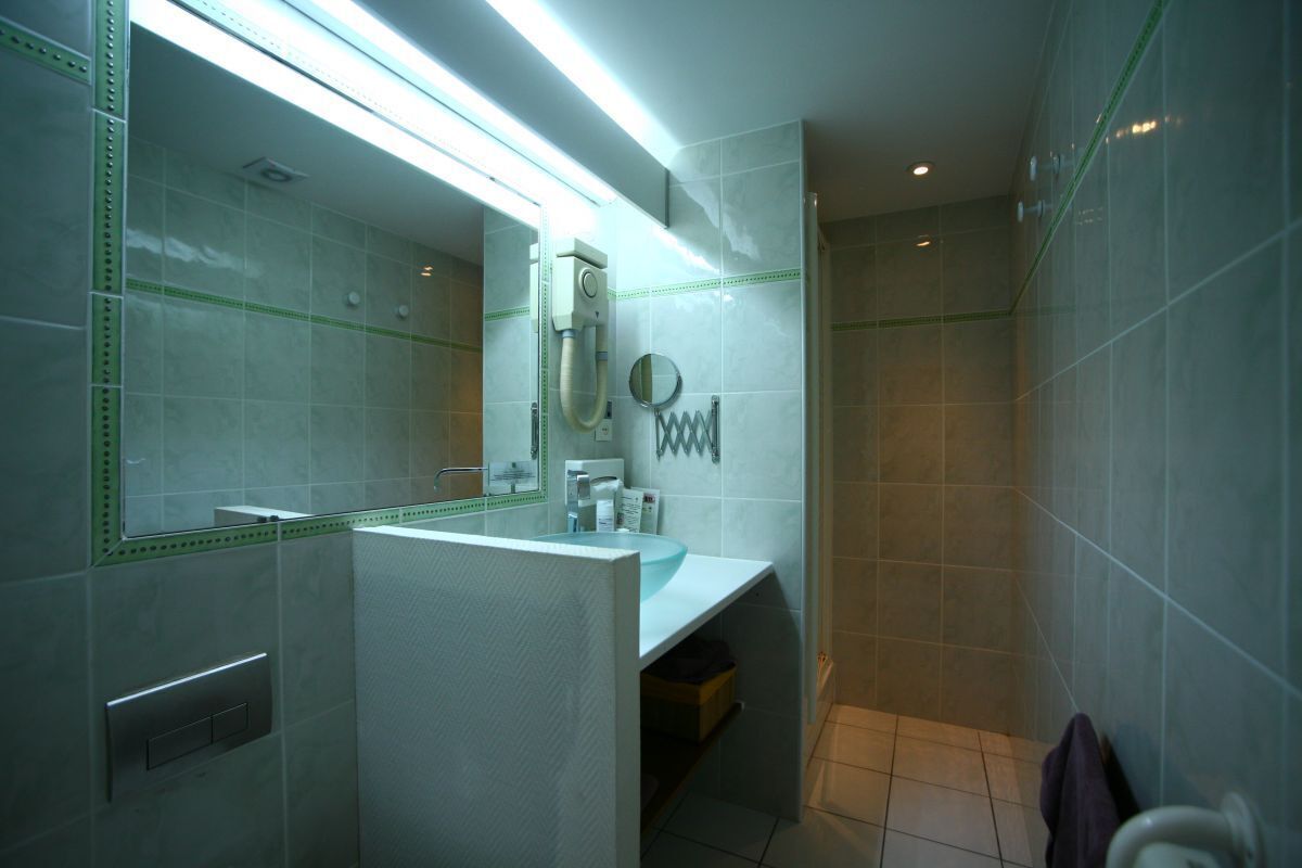 A modern bathroom with a white sink, a mirror, and a shower area.