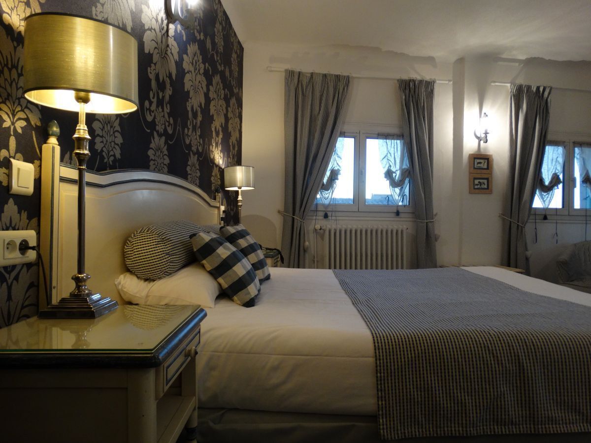 Una habitación de hotel con una cama grande, dos lámparas de noche, una mesita de noche, una ventana con cortinas y un radiador.