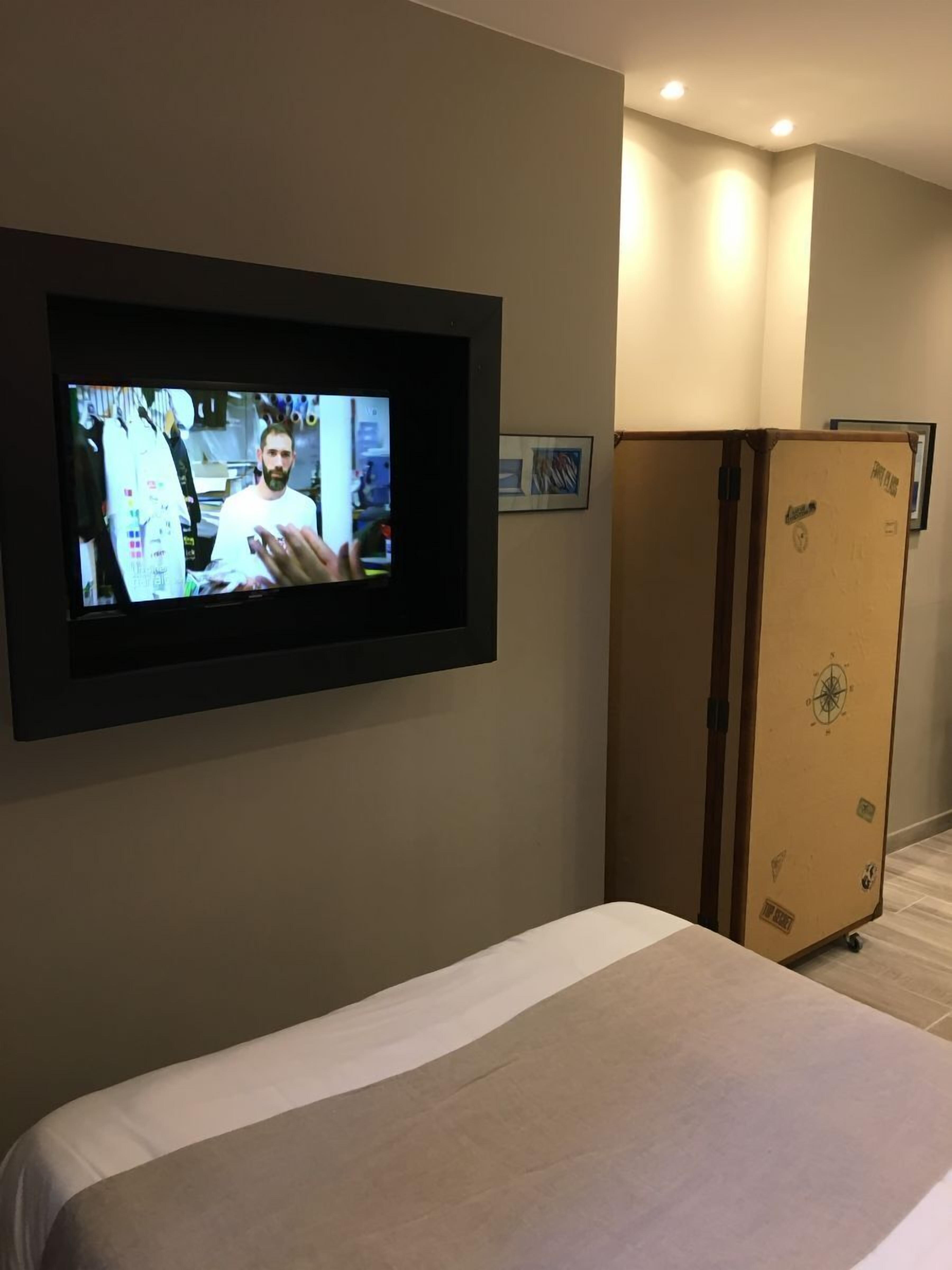 Ein Hotelzimmer mit Bett, einem an der Wand montierten Fernseher und einem Holzschrank.