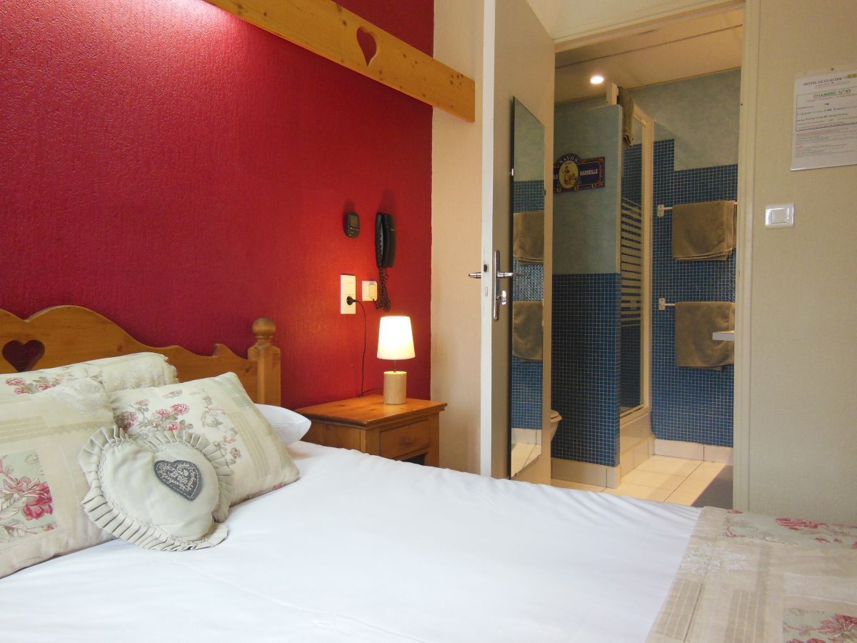 A hotel room with a bed, a nightstand with a lamp, a telephone, and a door leading to a bathroom with a blue tiled shower.