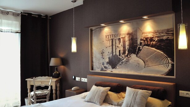 A modern hotel room with a large bed, a side table with a lamp, and a large framed picture on the wall. - Logis Hôtel Le Glacier (Orange)