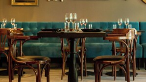 A dining area with wooden chairs and tables, a teal sofa, and decorative mirrors on the wall. - Logis Hôtel Le Glacier (Orange)