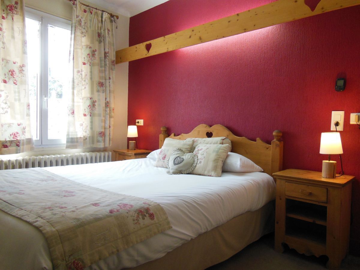 A bedroom with a bed, two bedside tables, a window with curtains, and a radiator.