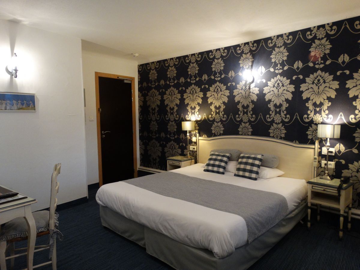 Camera d'albergo con un letto grande, due comodini con lampade, una scrivania e una sedia, e una porta.