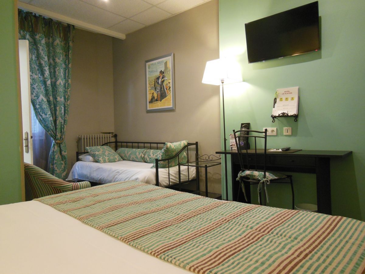 Habitación de hotel con dos camas individuales, un escritorio, una silla, un televisor y una lámpara.